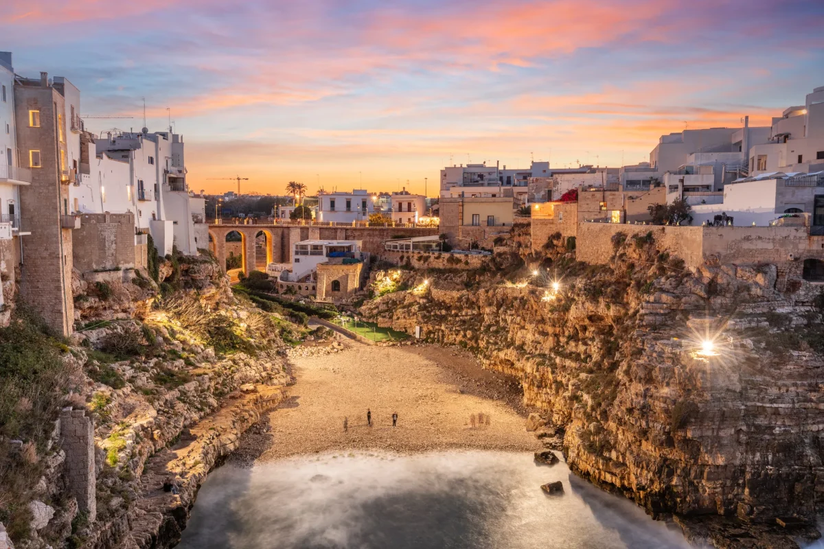 Polignano a Mare al tramonto, con le luci del borgo sopra la cala e la spiaggia